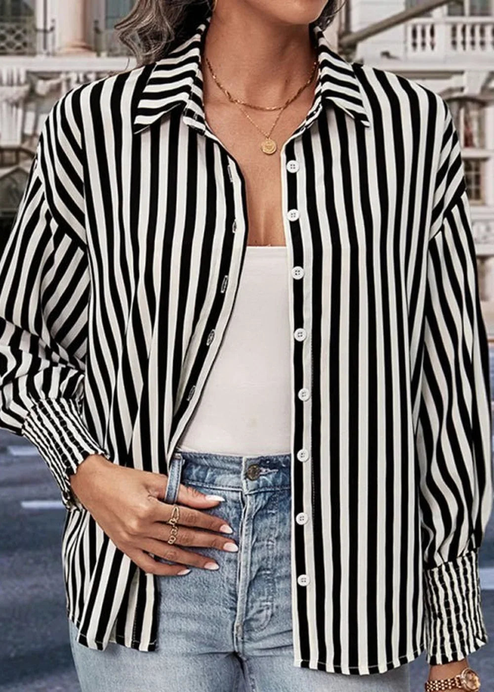 Black and white striped button-up shirt with gold necklace and blue jeans on model.