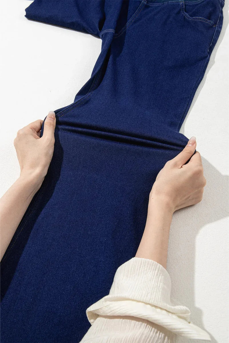 Close-up of hands stretching navy blue denim fabric, showing moderate stretch and cotton-polyester-elastane blend.