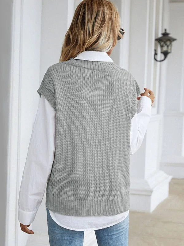 Back view of a woman wearing a grey knit sweater vest over a white collared shirt.