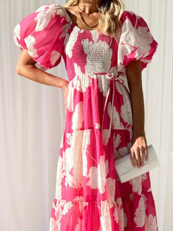 Pink floral print tiered maxi dress with puffy sleeves and a white clutch.