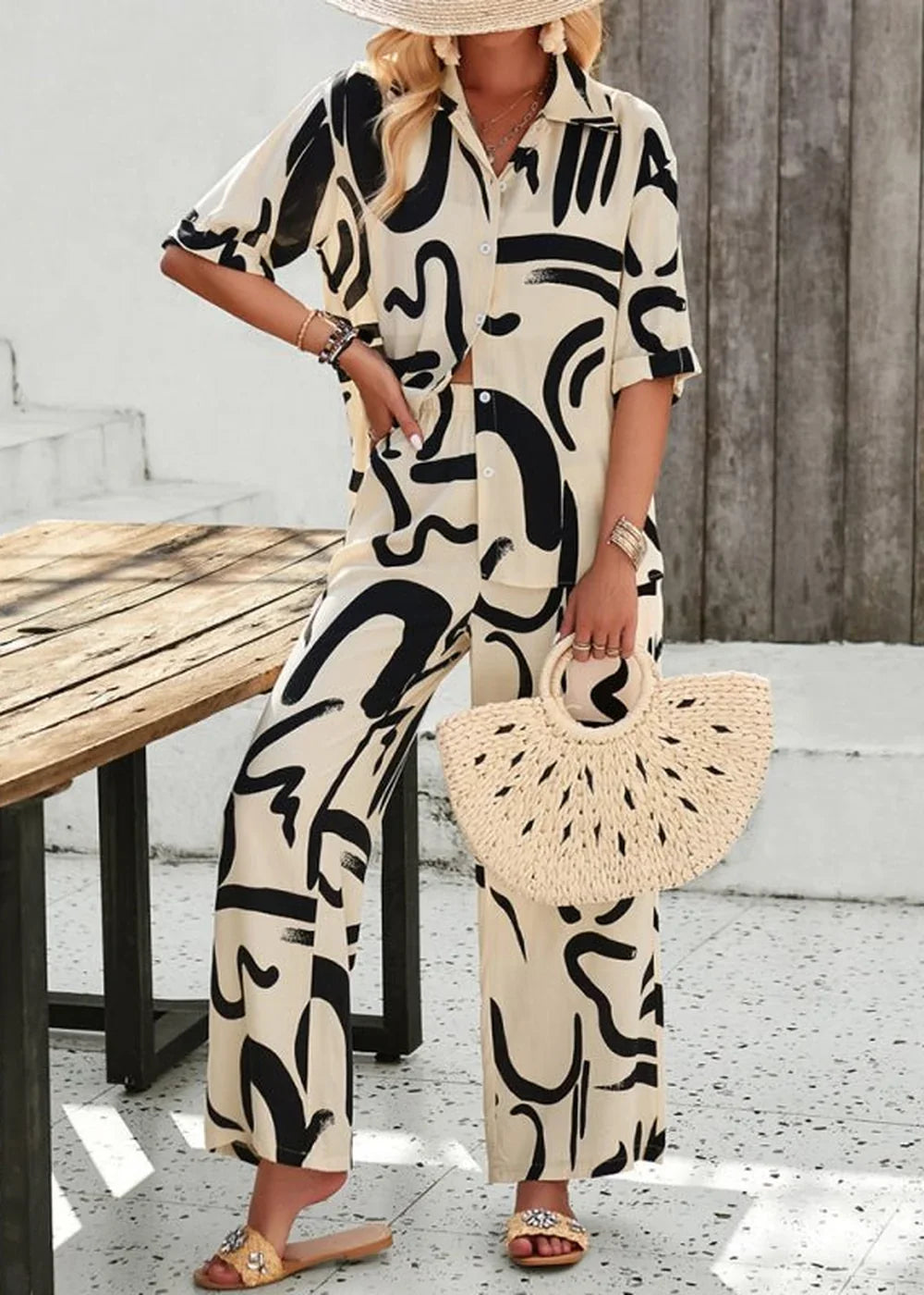 Champlain color pant suit with abstract black print, wide legs, and straw bag.