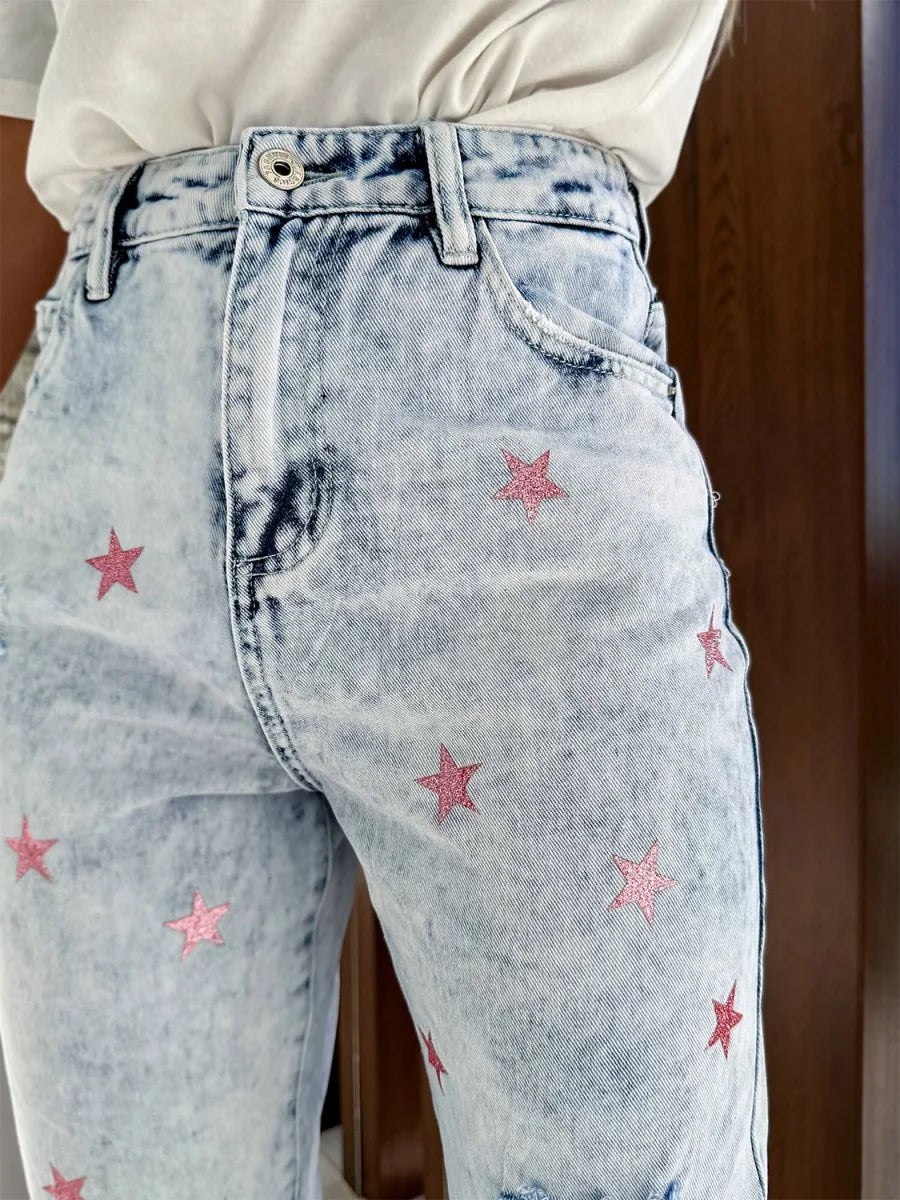 Light wash denim jeans with pink glitter star pattern and frayed hem detail.
