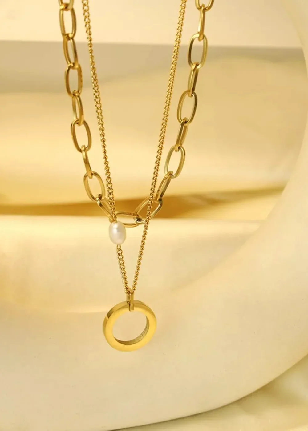 Gold-toned layered necklaces with a pearl and circular pendant.