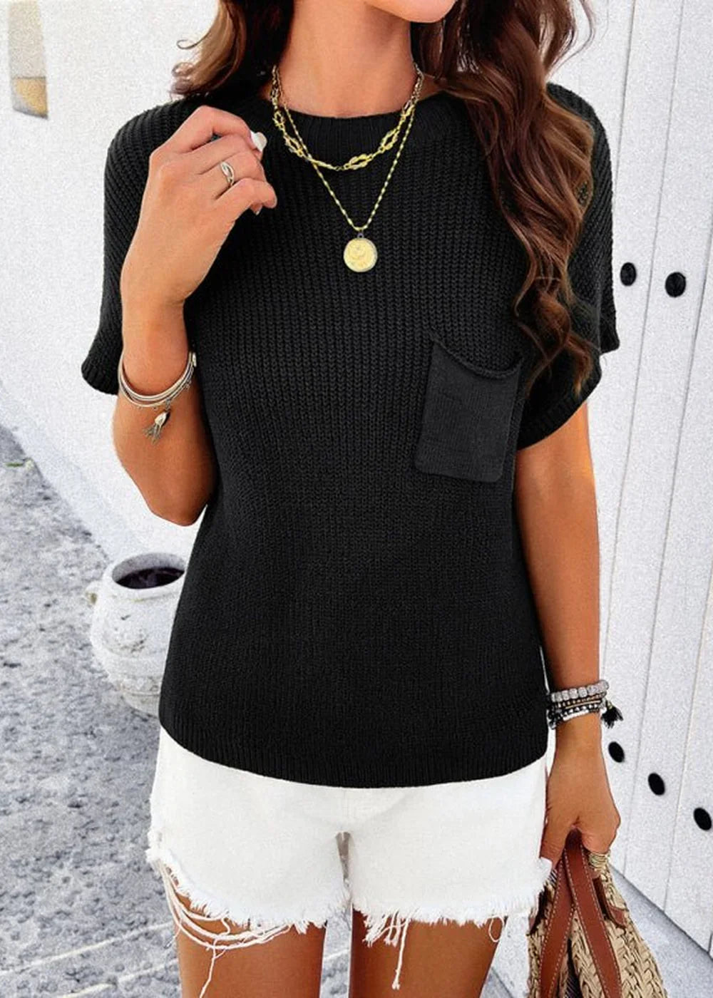 Black knit short-sleeve top with a chest pocket, layered gold necklaces, and white distressed denim shorts.