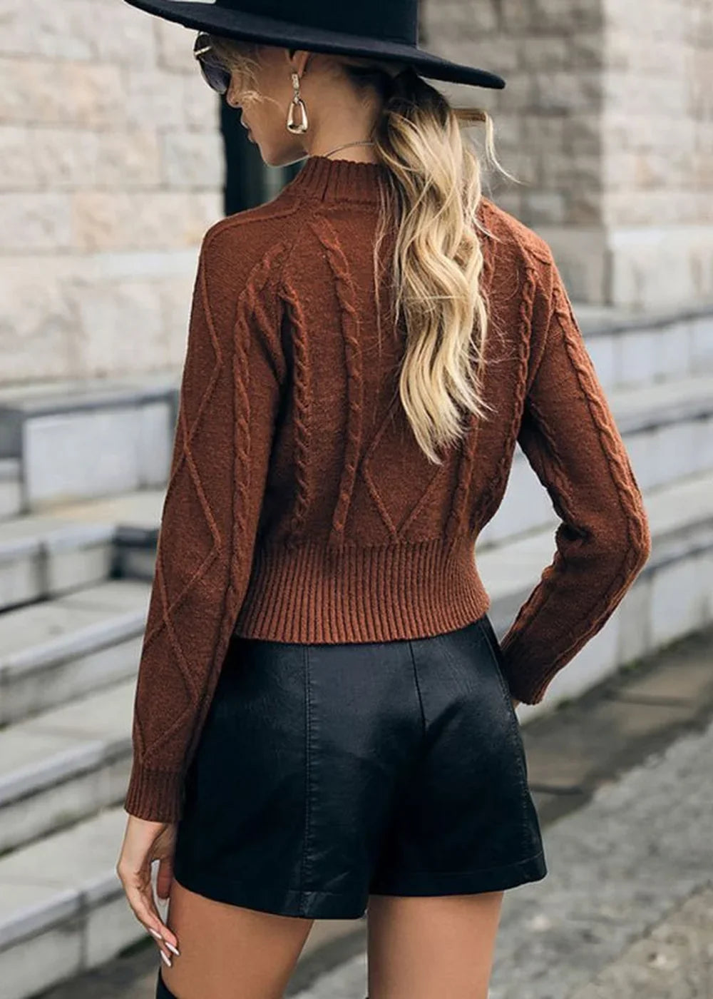 Brown cable-knit cropped sweater with black faux leather shorts on model.