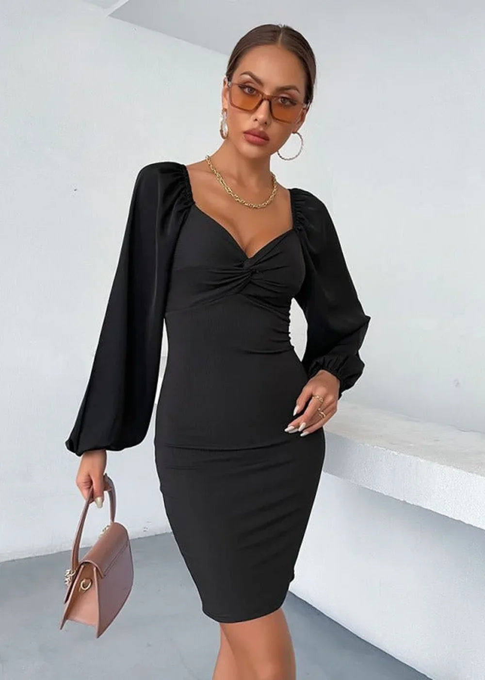 Black ruched sweetheart neckline dress with voluminous sleeves, worn by a model holding a brown handbag.