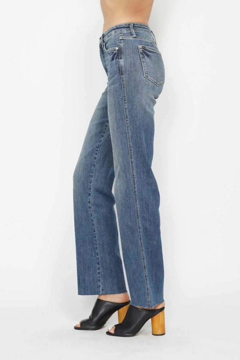 Side view of medium wash, straight-leg jeans with frayed hem, worn by a model with black heeled mules.