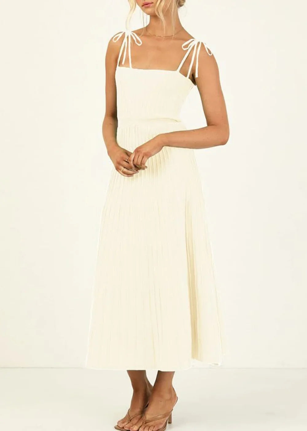 Cream knit midi dress with tie straps and a pleated skirt, shown on a model.