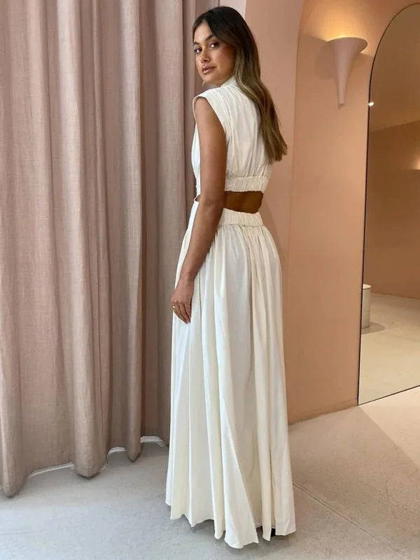 Cream sleeveless maxi dress with cutouts at the waist and a high neckline, shown on a model.