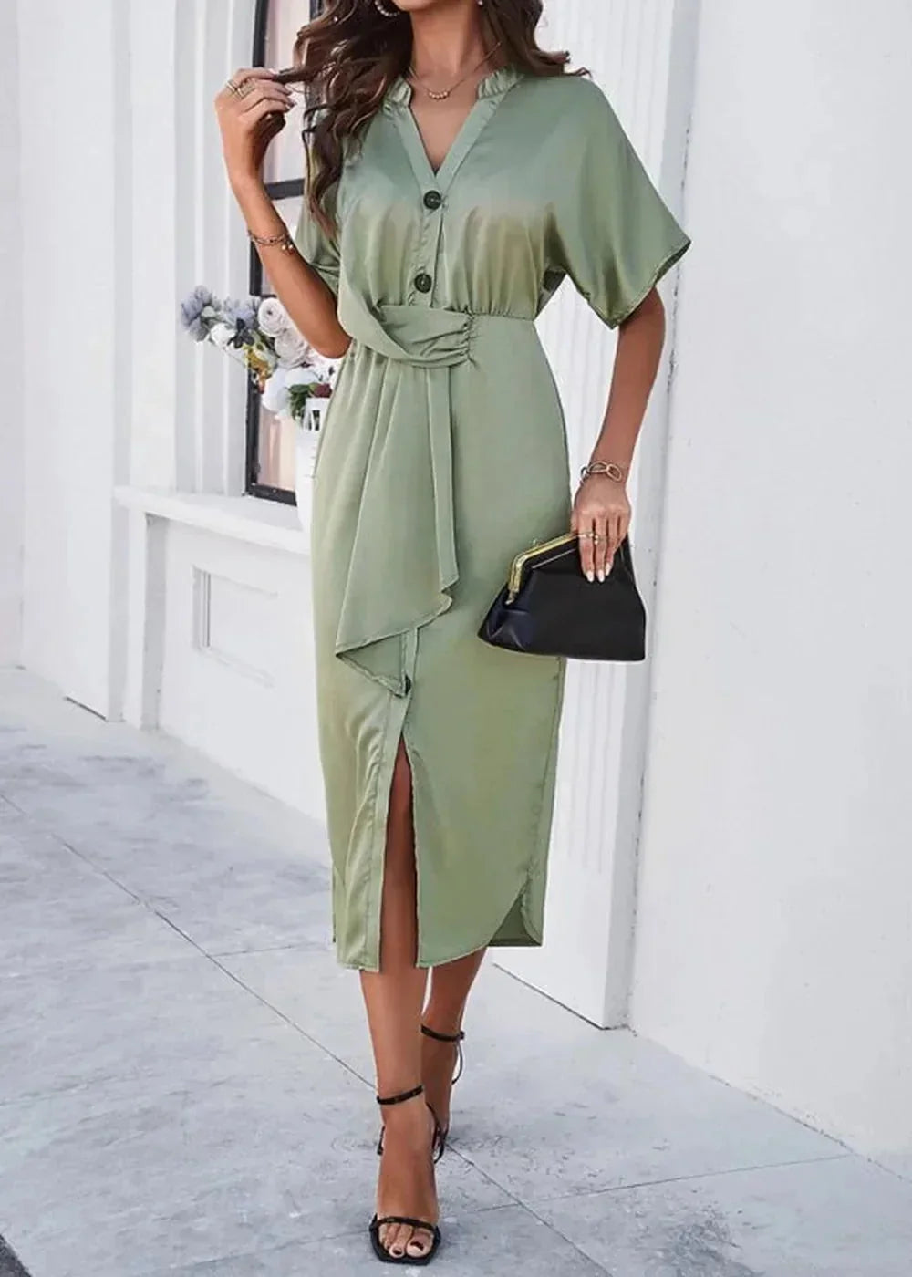 Sage green satin dress with tie waist and high slit, worn by a model with black heels and clutch.