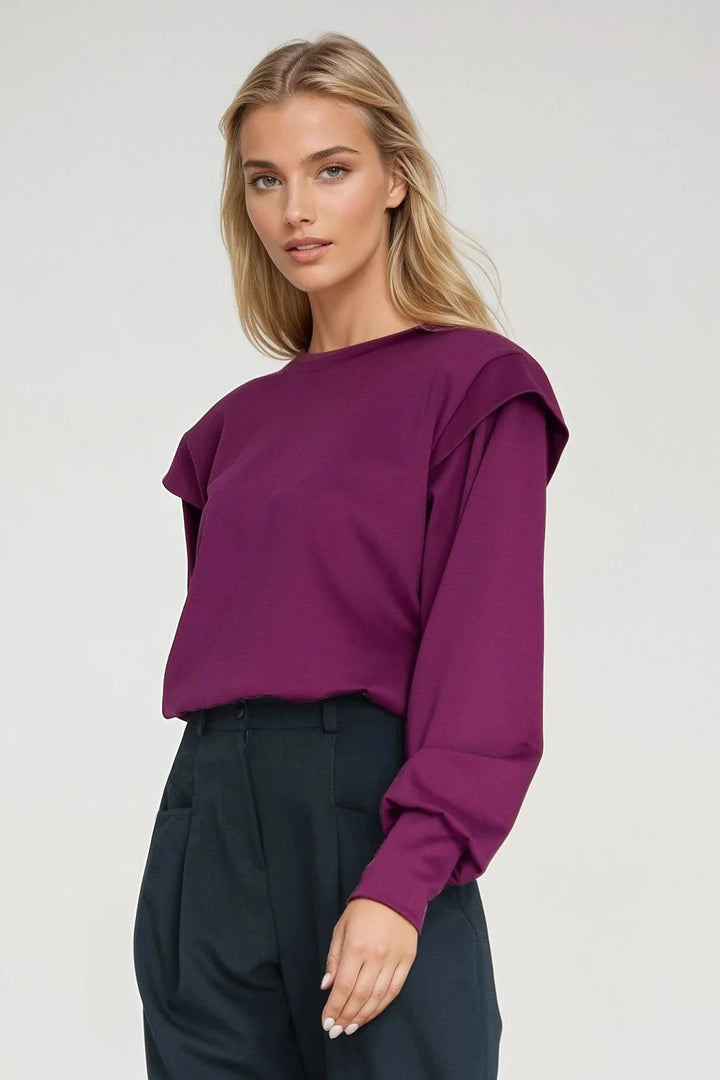 Deep magenta long-sleeve top with layered shoulder detail, worn with dark green wide-leg trousers.