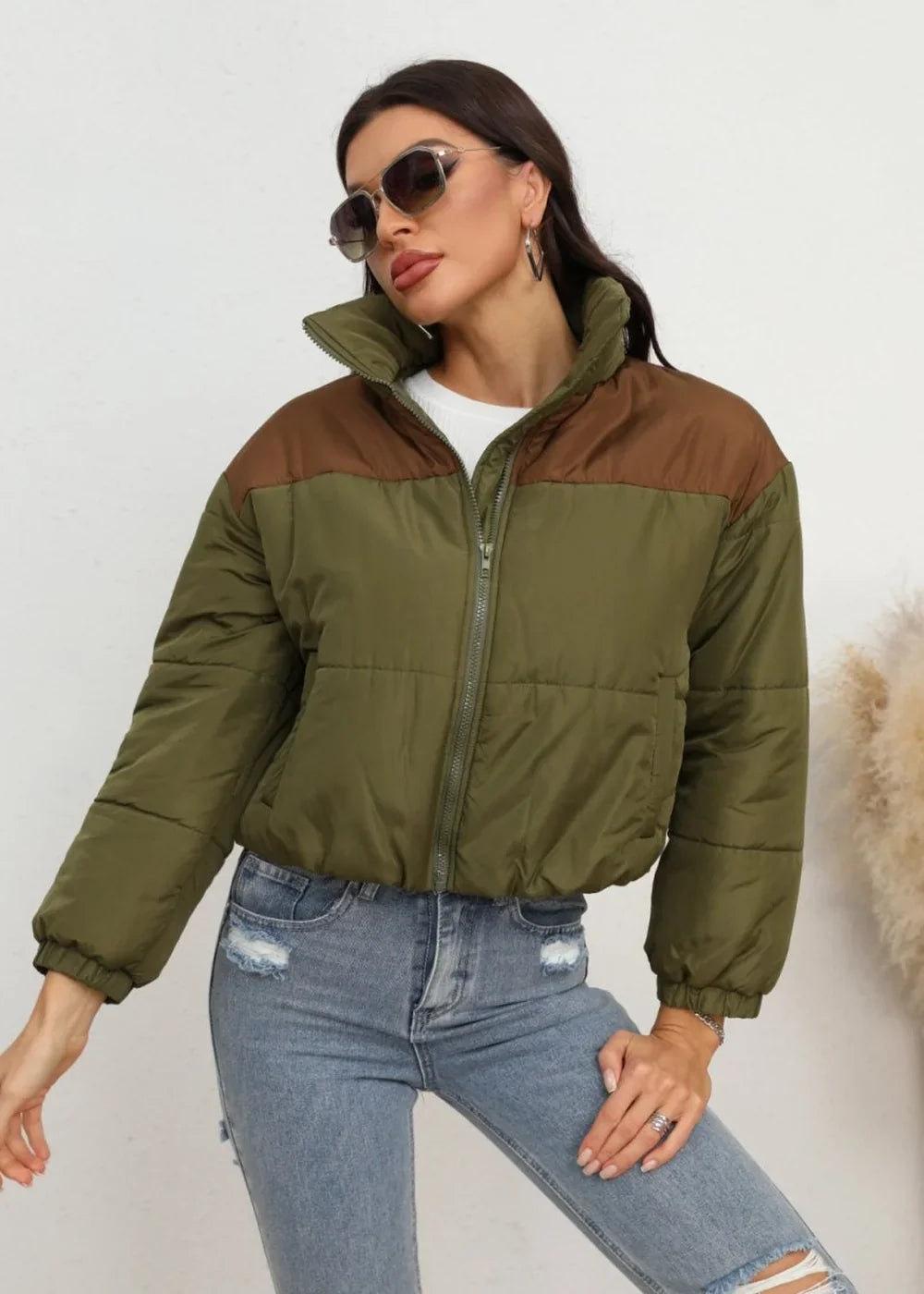 Olive green and brown color-blocked puffer jacket with a high collar, worn by a model with ripped blue jeans.