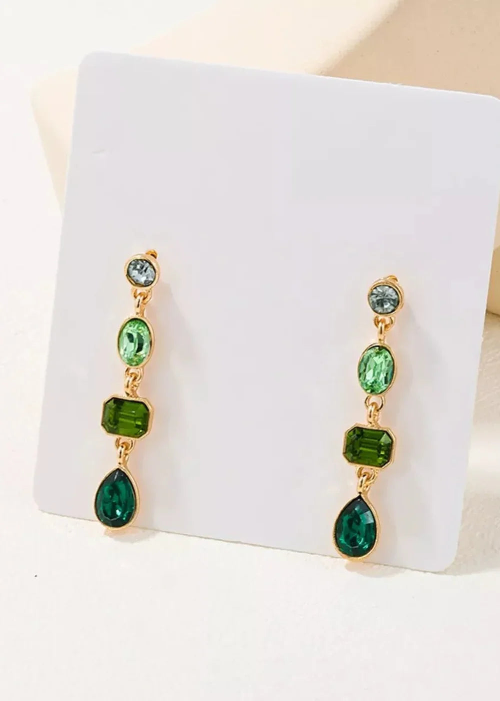 Gold-toned drop earrings with stacked green acrylic gems in round, oval, and teardrop shapes.