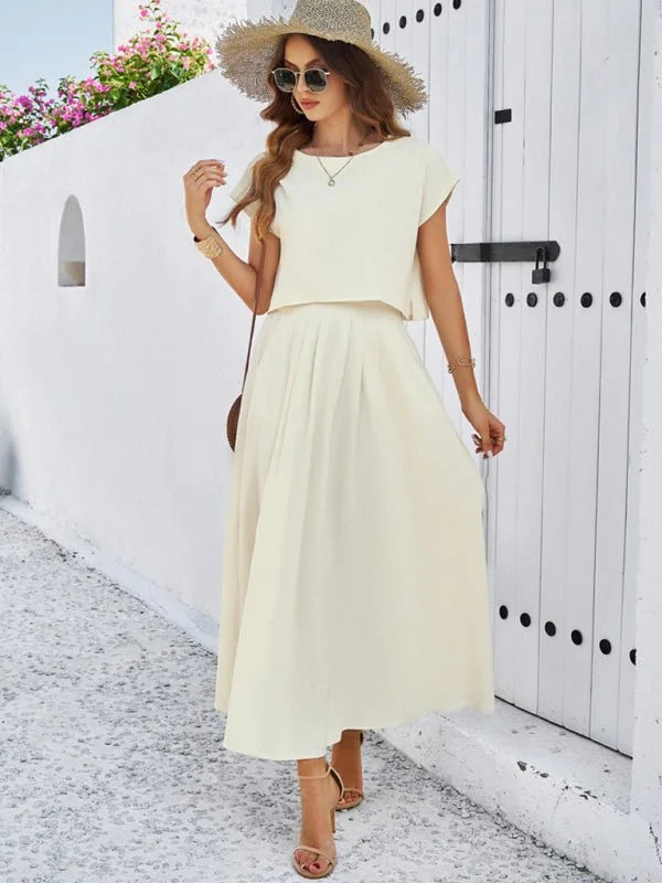 Cream-colored cropped top and pleated midi skirt suit with straw hat and sandals.