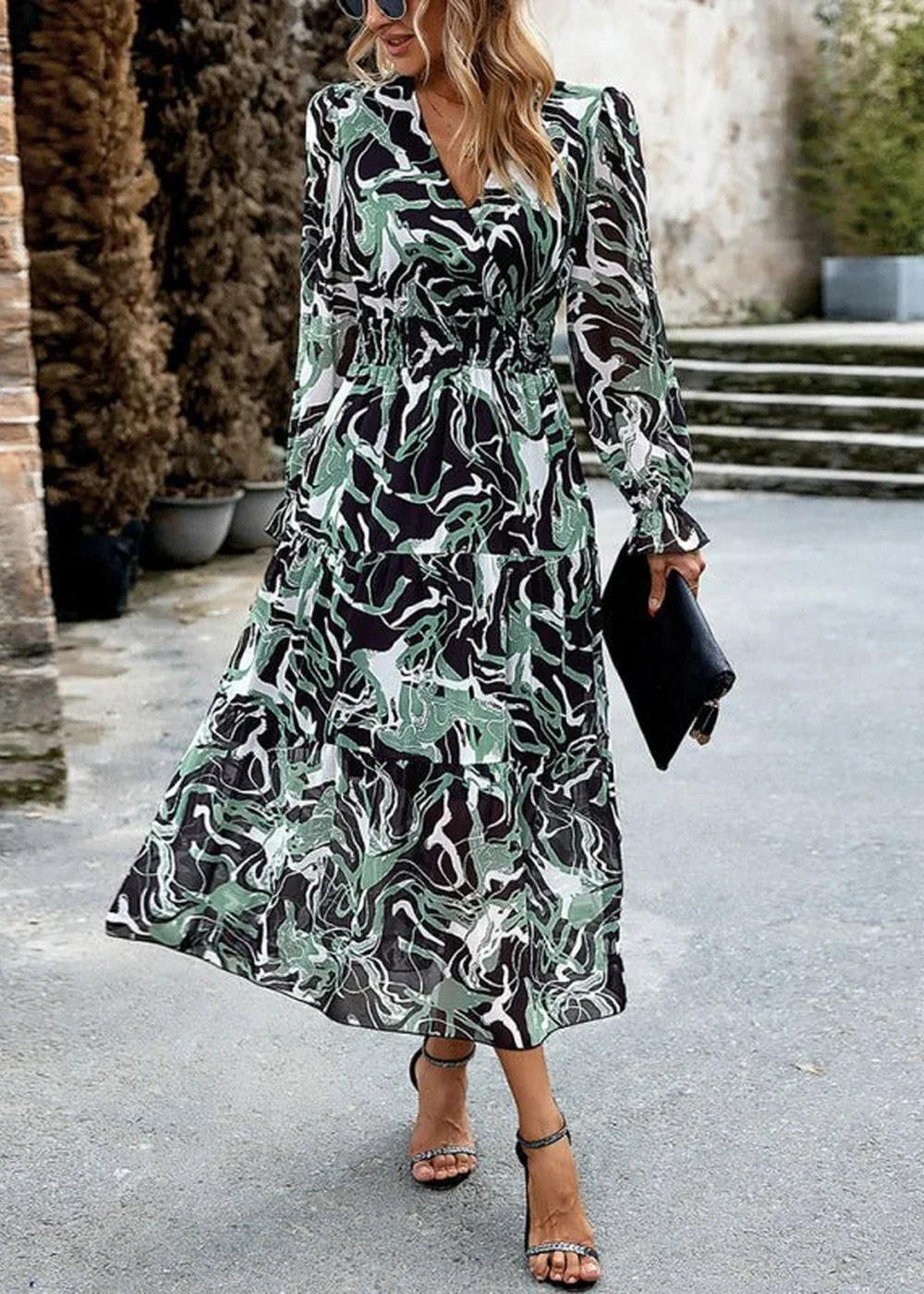 Flowy midi dress with a black, green, and white abstract print, V-neck, and tiered skirt.