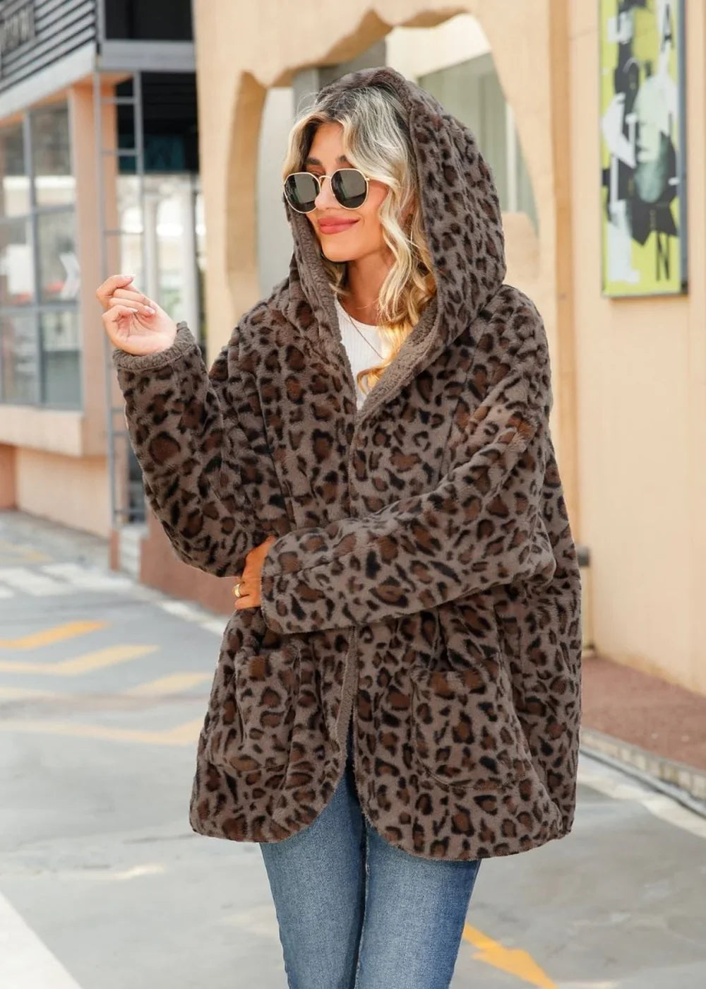 Woman wearing a cozy, hooded leopard print jacket with a soft texture, paired with blue jeans.