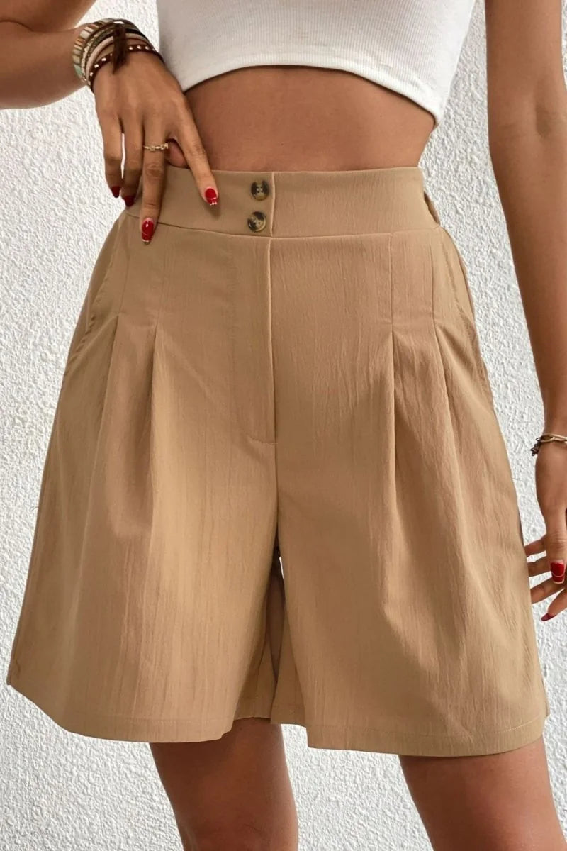 Tan pleated shorts with button closure and textured fabric, shown on model.