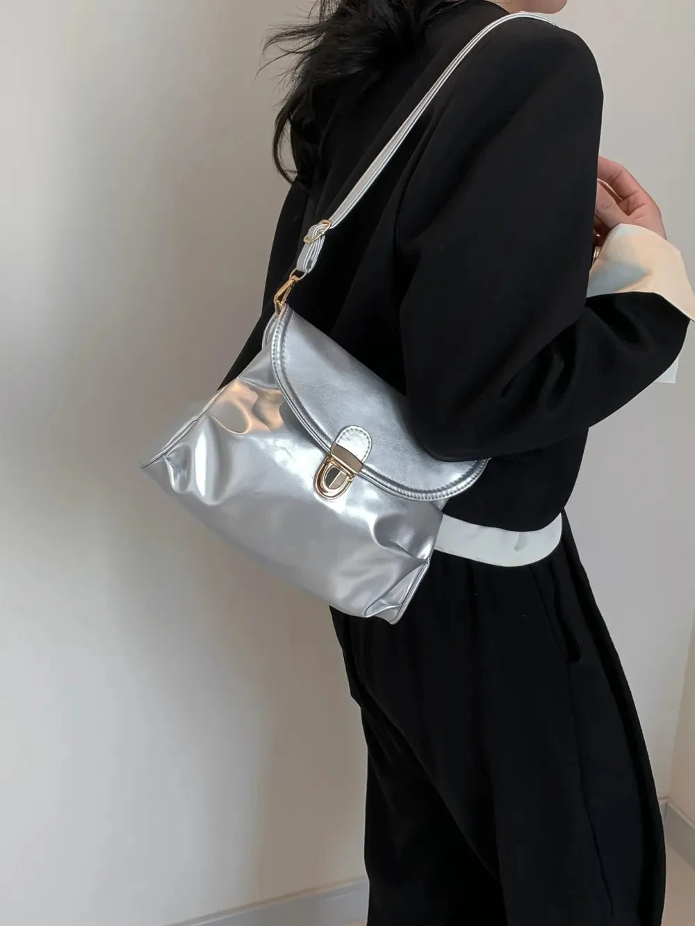 Silver metallic handbag with gold clasp and strap, worn with a black blazer.