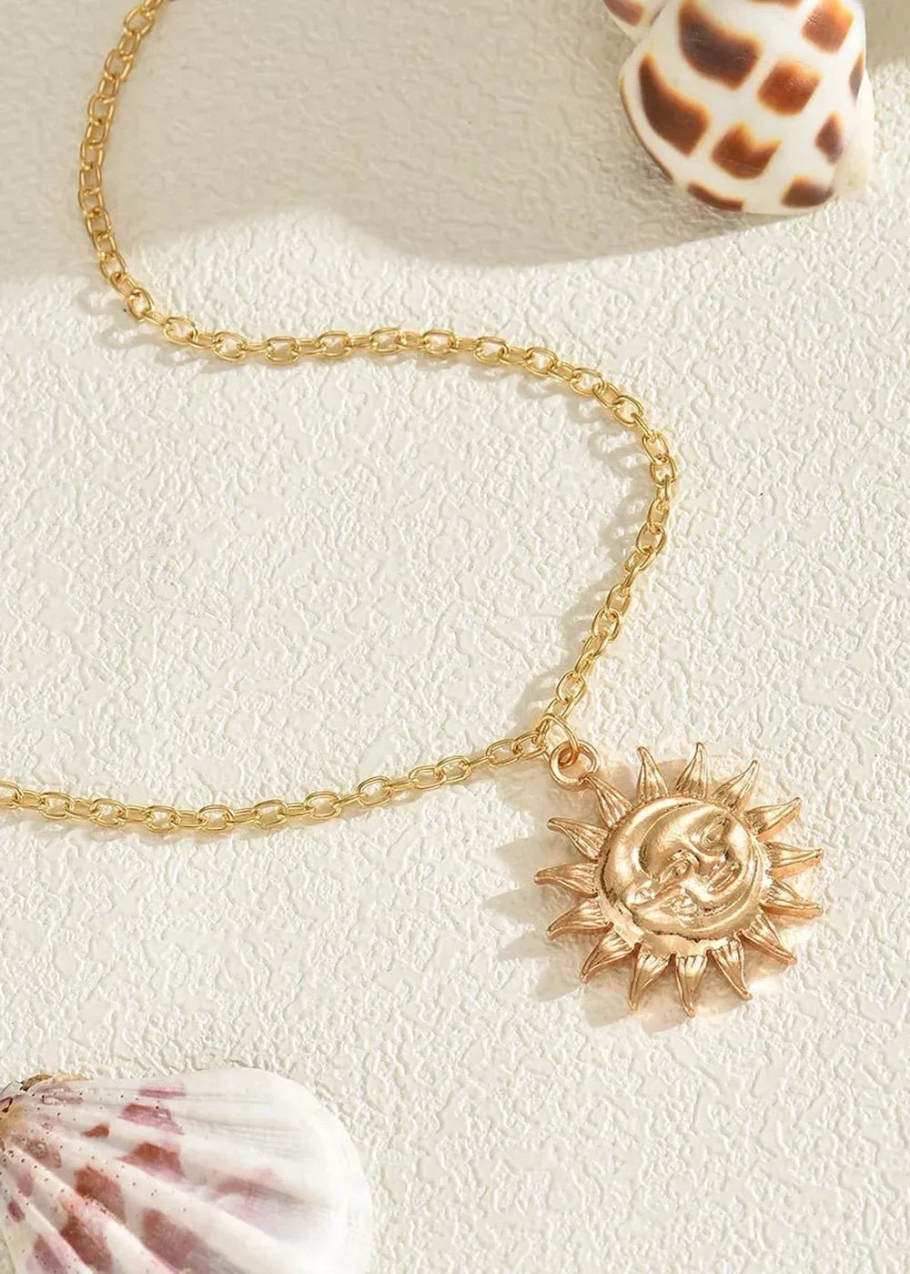 Close-up of a gold-plated sun and moon pendant necklace with a delicate chain, resting on a textured white surface.