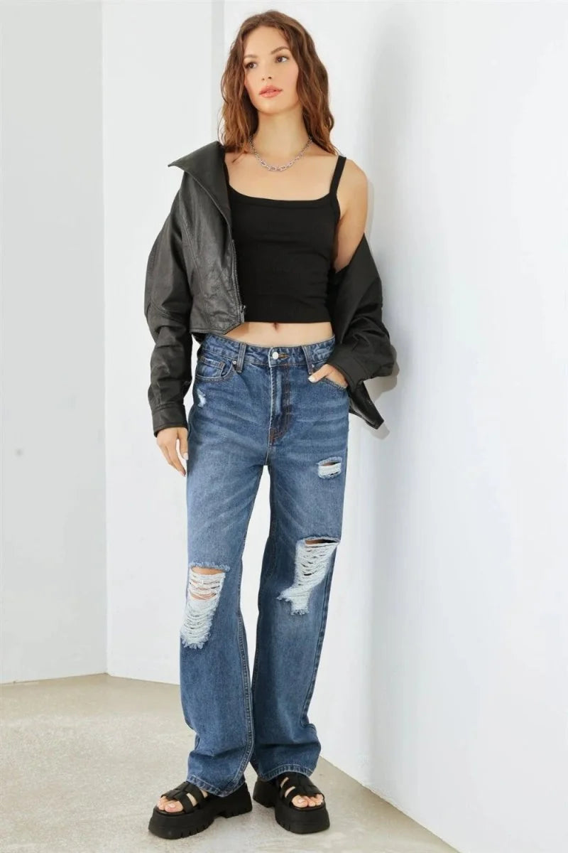 Distressed medium-wash denim jeans with a relaxed fit, featuring ripped knees and a frayed hem, worn by a model with platf...