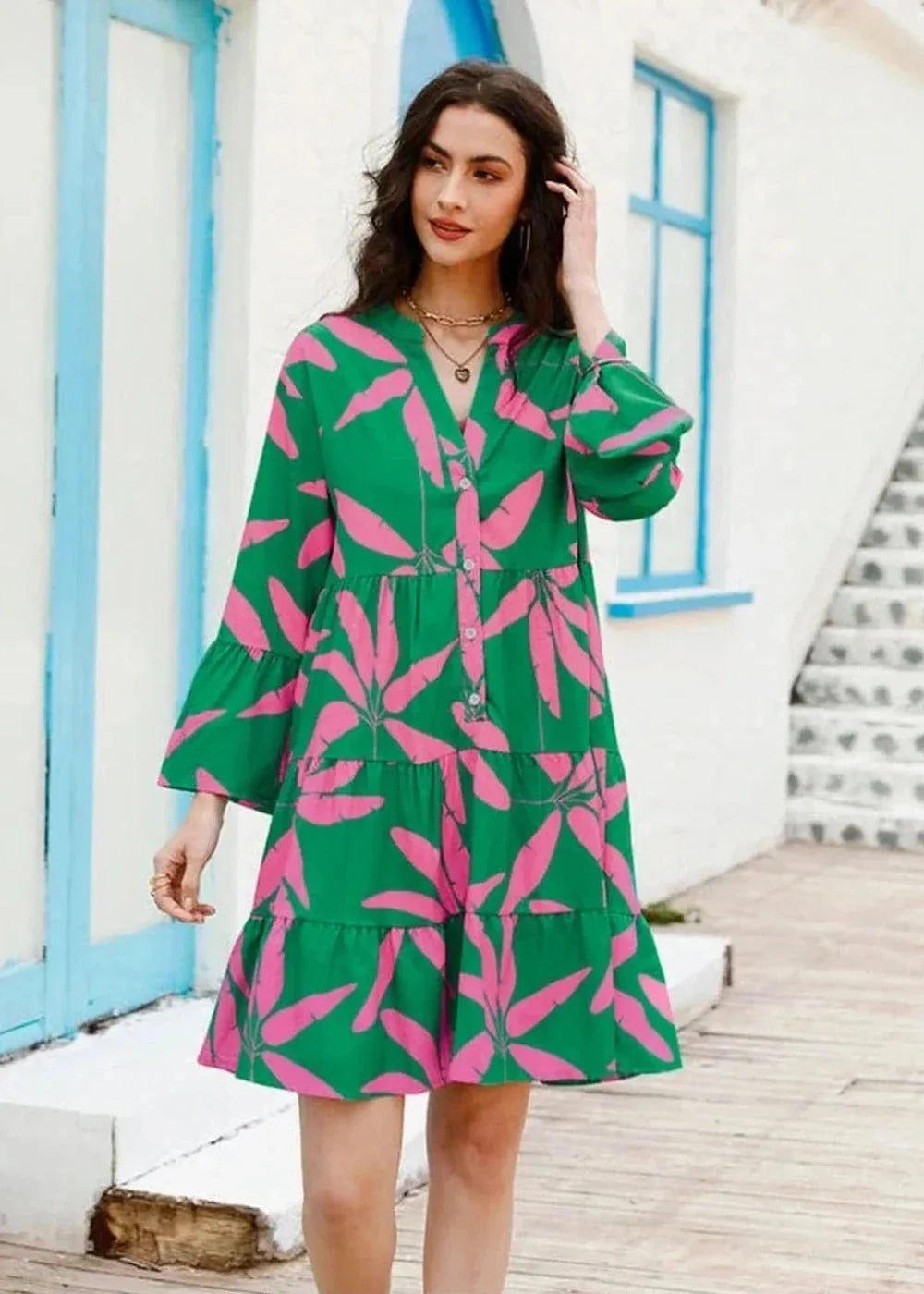 Green polyester dress with pink floral print, V-neck, tiered skirt, and bell sleeves on a model.