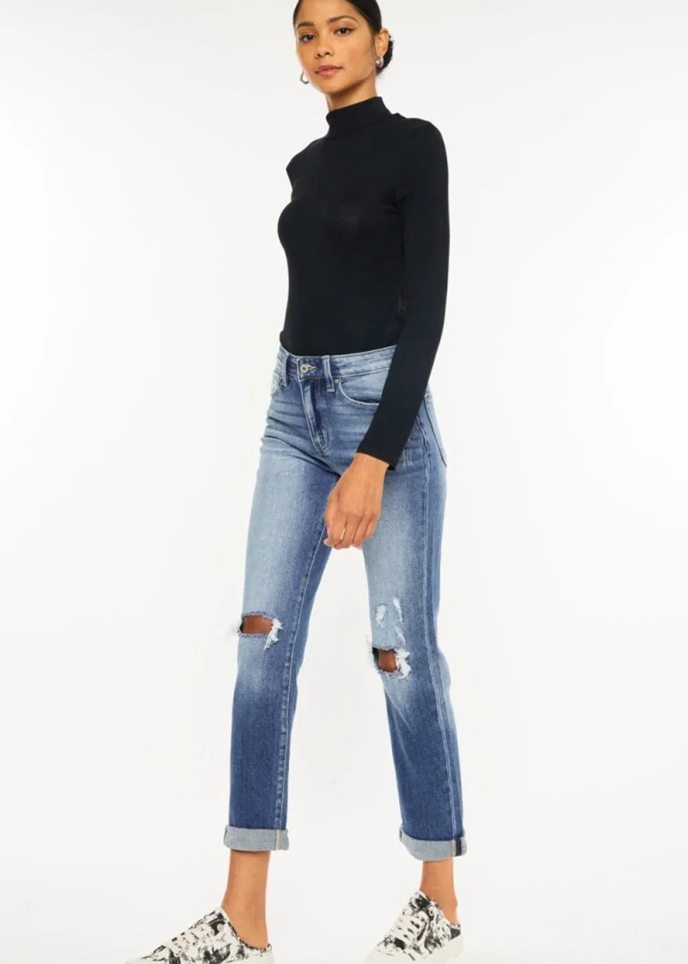 Distressed light wash denim jeans with rolled cuffs and ripped knees on a model.