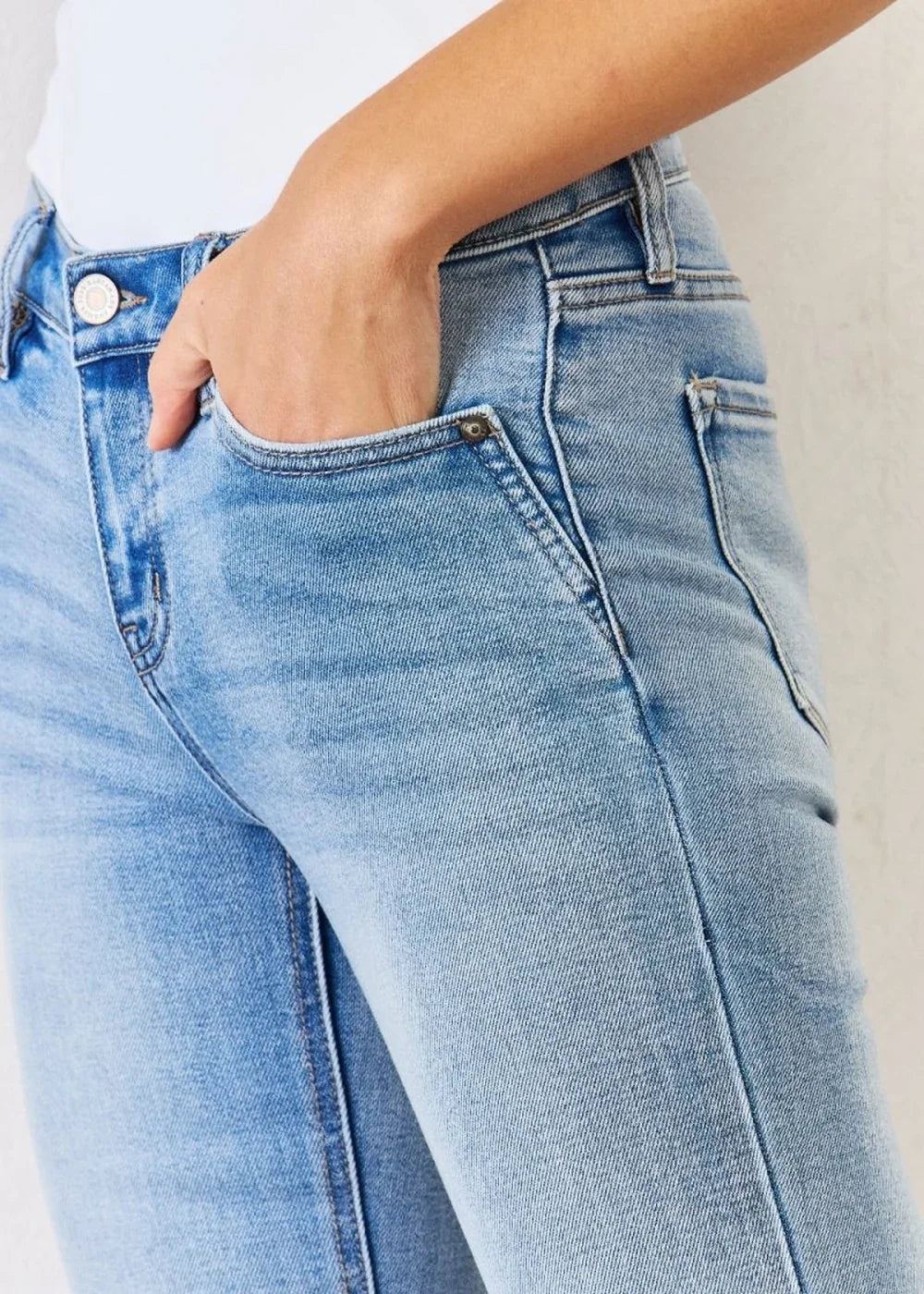 Close-up of light wash distressed denim jeans with a hand in the pocket.