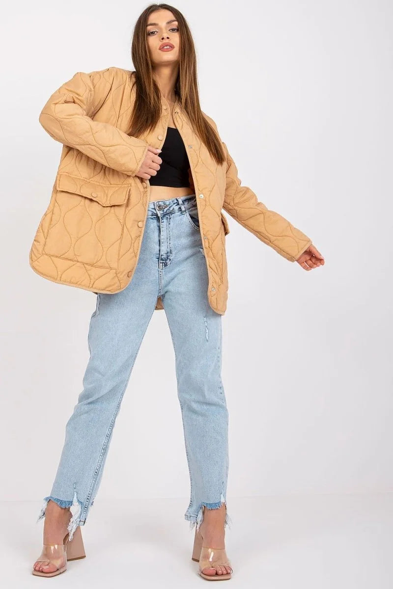 Quilted tan jacket with front pockets, worn by a model with light wash ripped jeans and clear heels.