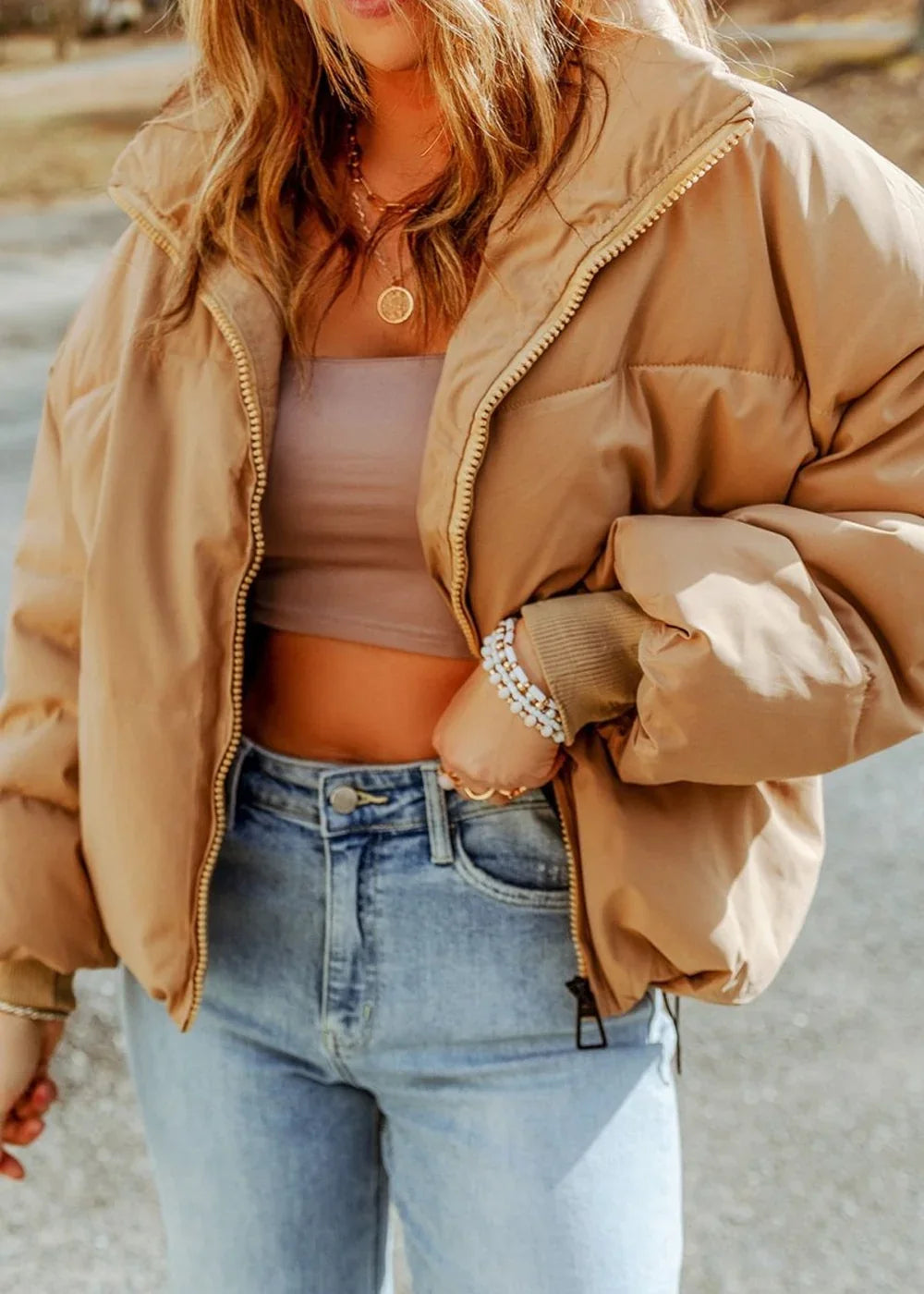 Tan puffer jacket with zipper closure and light wash jeans on a model.