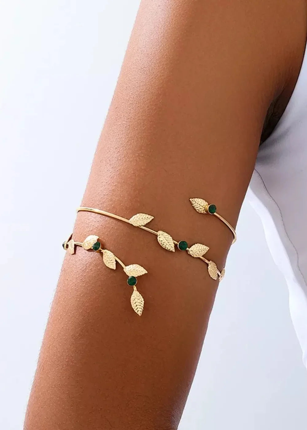 Gold arm cuff with leaf and emerald green stone accents on a tanned arm.