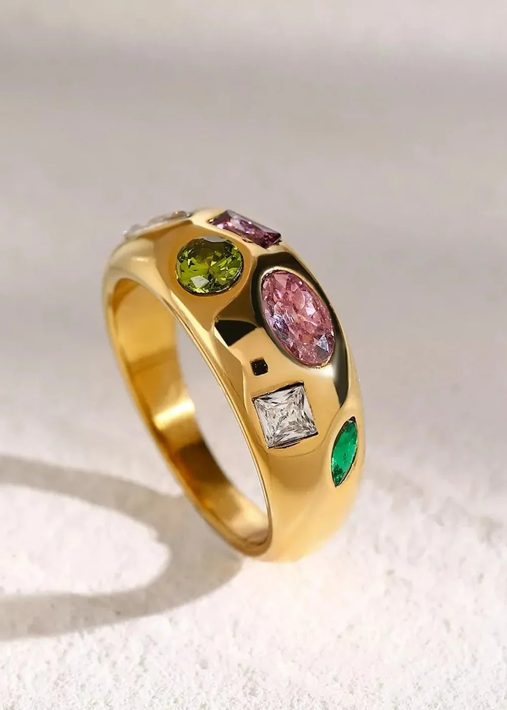 Gold ring with a dome band, featuring an assortment of colorful gemstones including pink oval, green round, white square, ...
