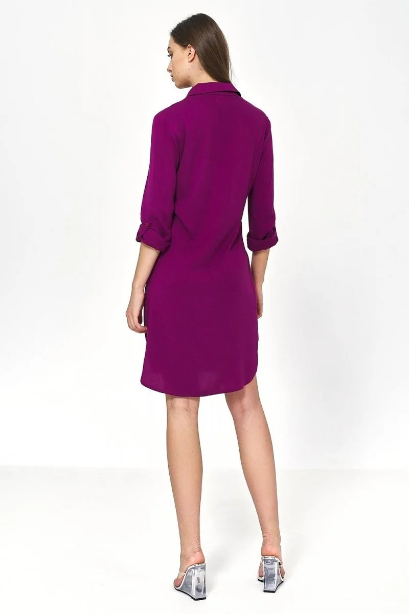Back view of a woman wearing a vibrant purple oversized viscose shirt dress with rolled-up sleeves and clear wedge sandals.