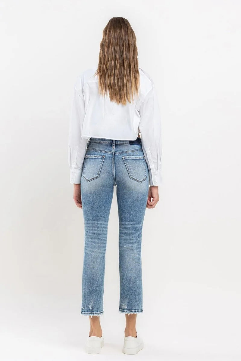 Back view of light-wash distressed denim jeans with frayed hems on a model.