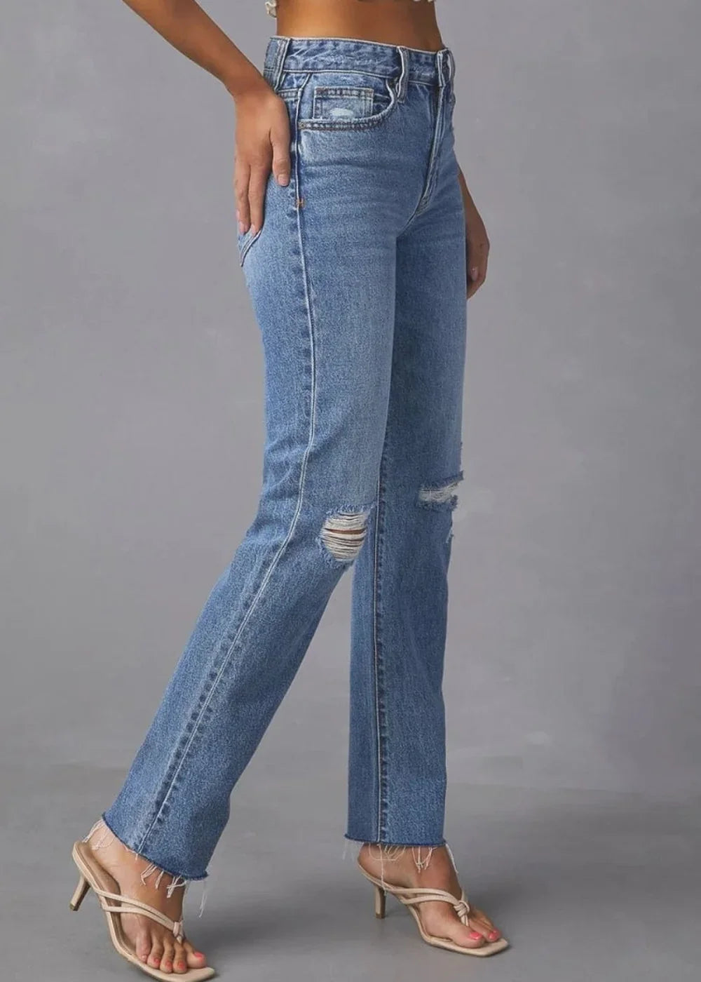 Distressed medium-wash denim jeans with frayed hem and high-rise fit.