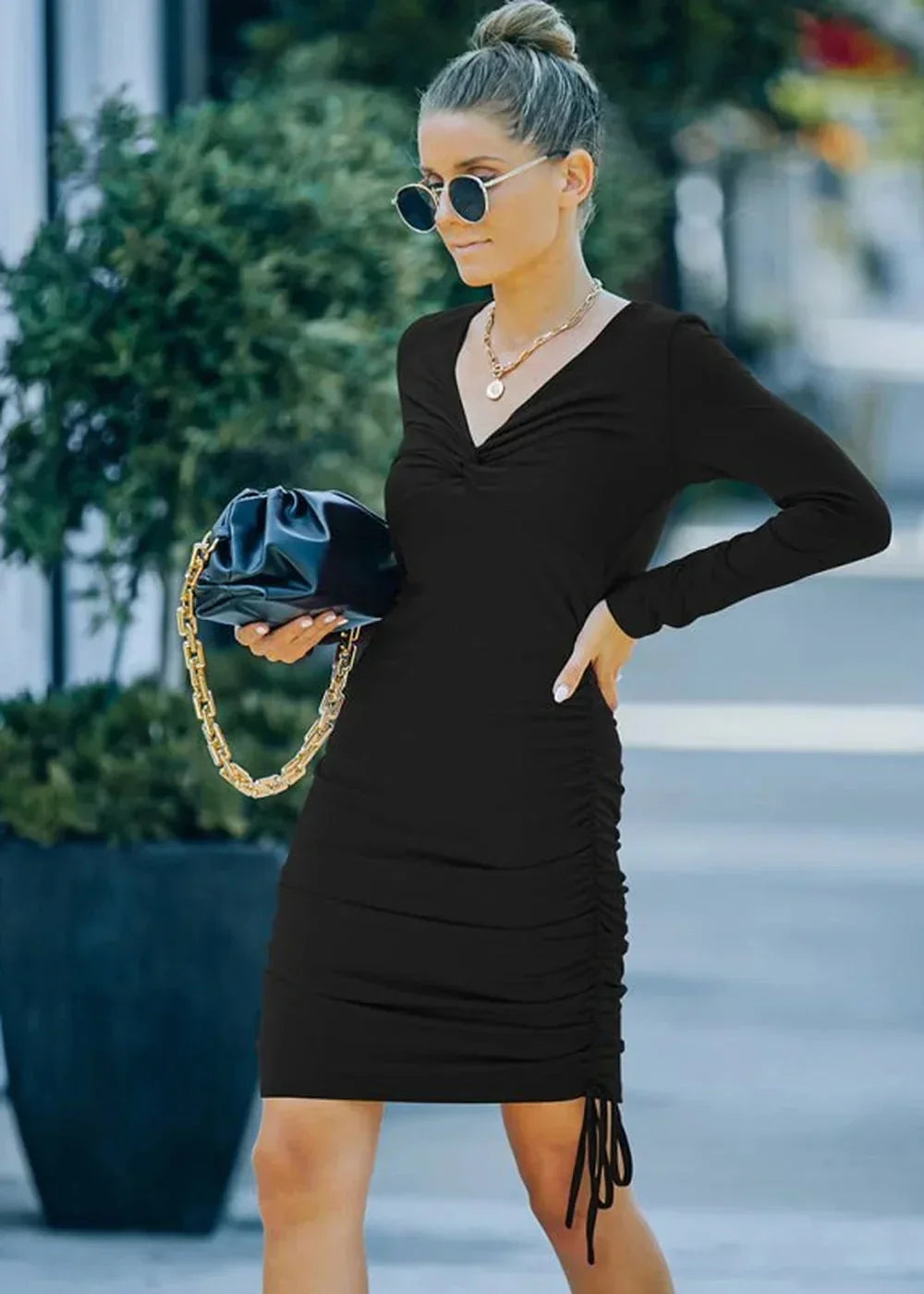 Black ruched long-sleeve dress with a V-neck, worn by a model holding a black clutch with a gold chain.