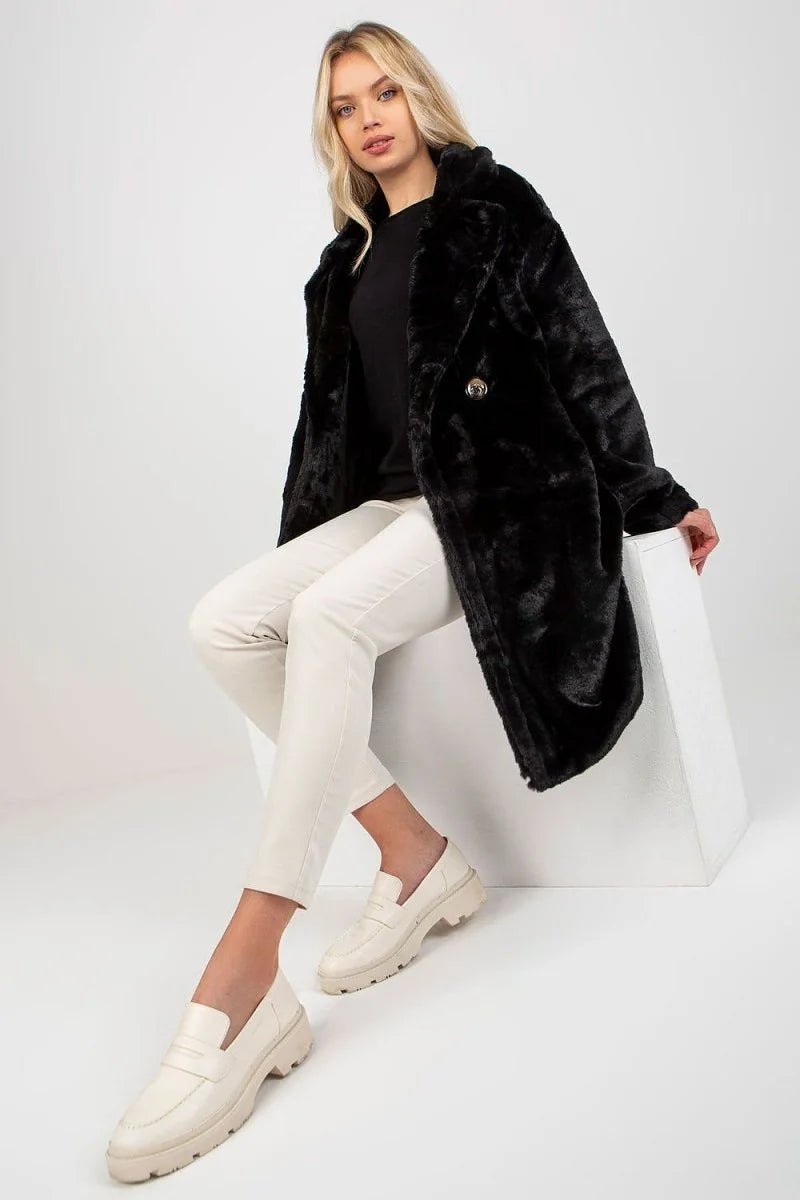 Woman in black faux fur coat and cream pants, wearing cream loafers.