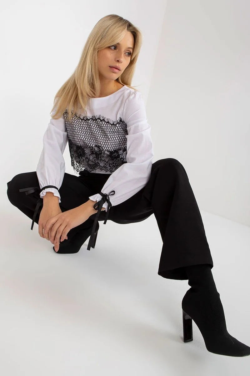 Woman in white long-sleeve top with black lace detail and black wide-leg pants, crouching.