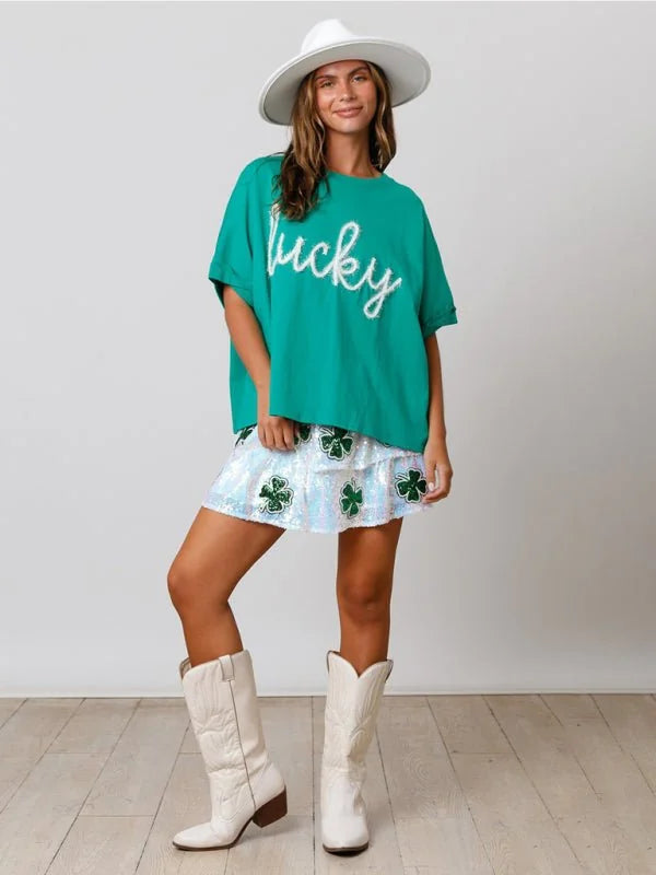 Green "lucky" graphic tee with sequined shamrock skirt and white cowboy boots