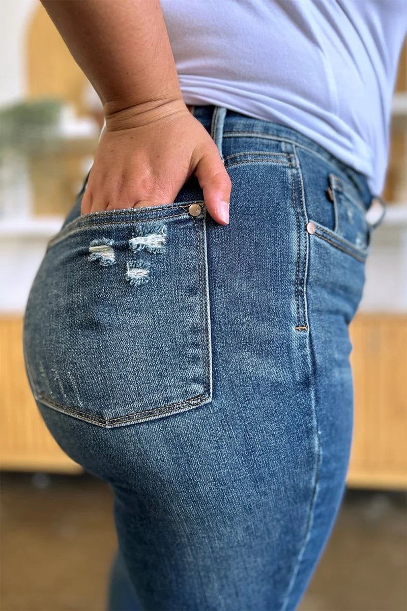 Close-up of distressed denim jeans with ripped pockets and a hand in the back pocket.