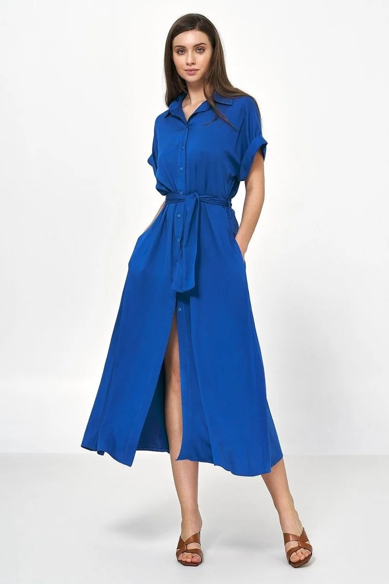 A woman in a royal blue viscose shirt dress with a belted waist and a thigh-high slit, paired with brown slide sandals.