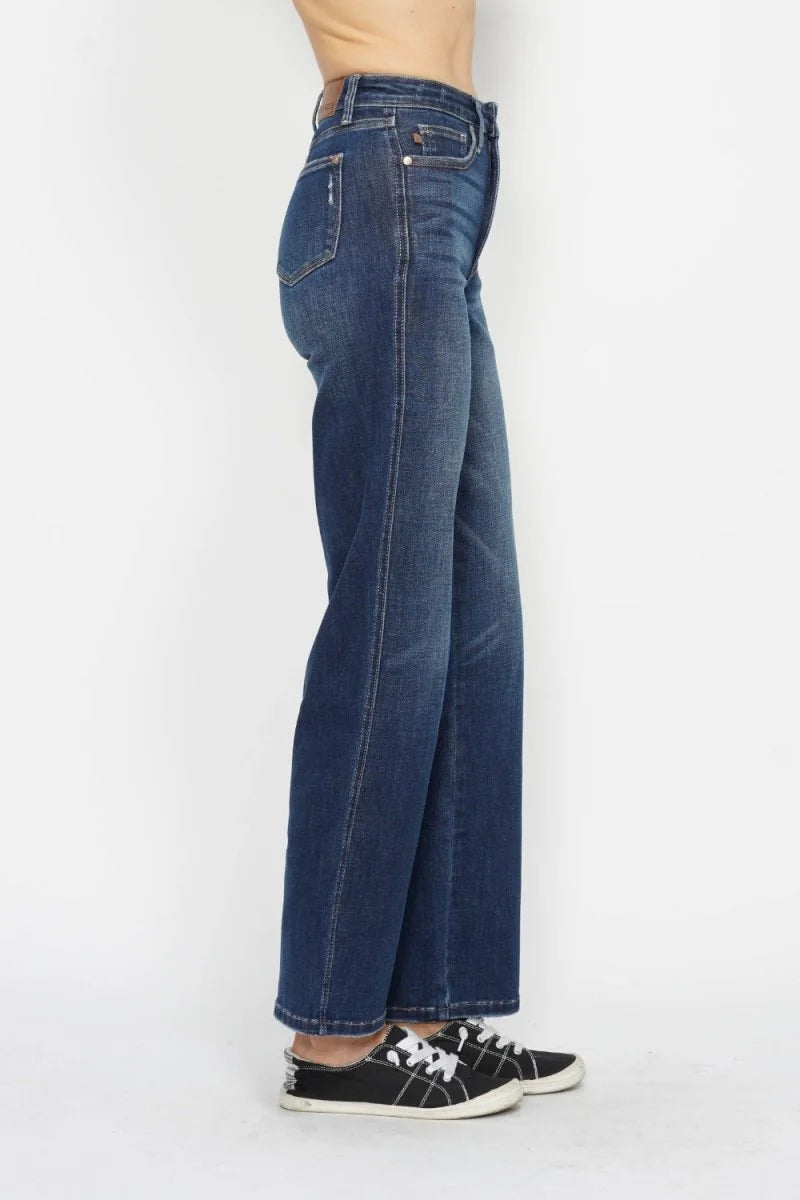 Dark wash, wide-leg jeans with a distressed detail on the left pocket and white stitching, shown on a model wearing black ...