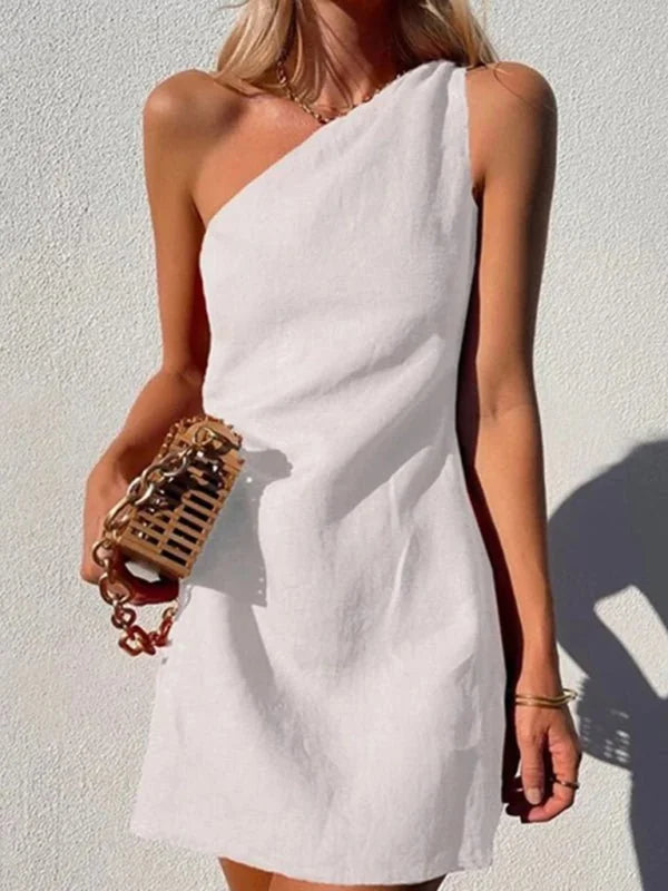 White one-shoulder mini dress with a textured, woven gold chain bag, shown on a model.