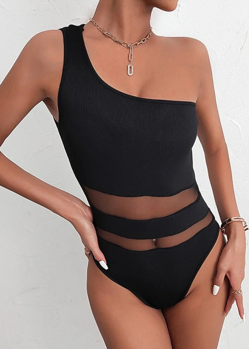 Black one-shoulder swimsuit with mesh cutouts and gold chain necklace on model