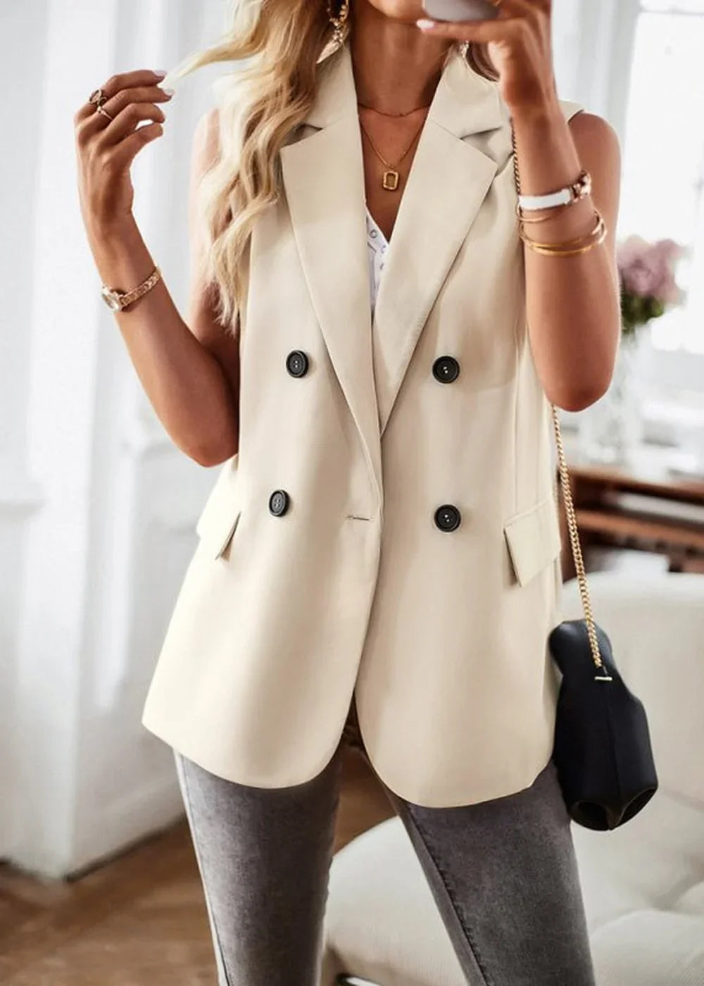 Cream double-breasted sleeveless blazer with black buttons, worn by a model with jewelry and a black handbag.