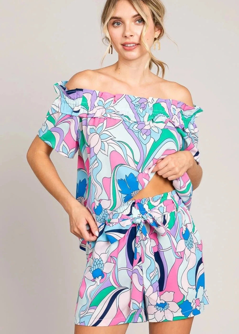 Off-the-shoulder romper with vibrant abstract floral print in pink, blue, green, and purple.