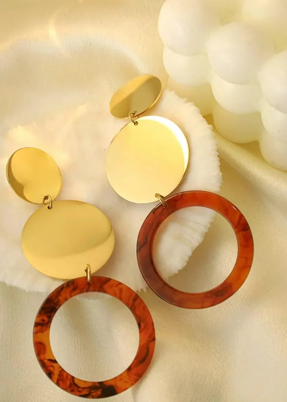 Gold geometric discs with brown marbled resin hoops on a cream textured background.