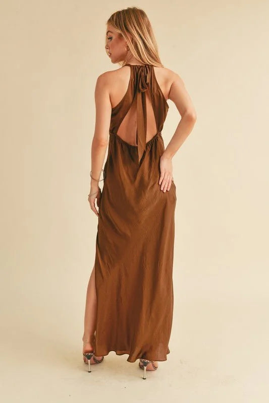 Woman in a flowing, backless brown maxi dress with a high slit, showing off her legs and heels.