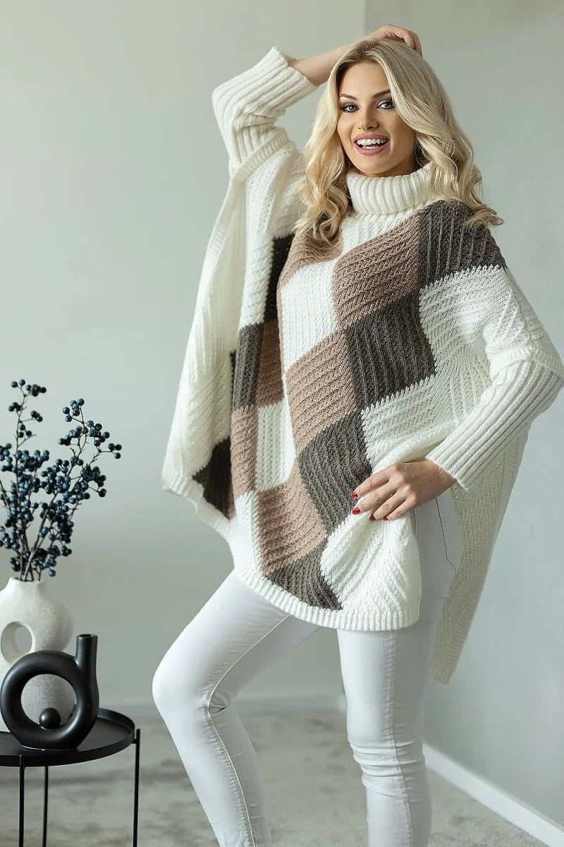 Cream and brown patchwork knit poncho sweater with turtleneck, worn by a blonde model in white pants.