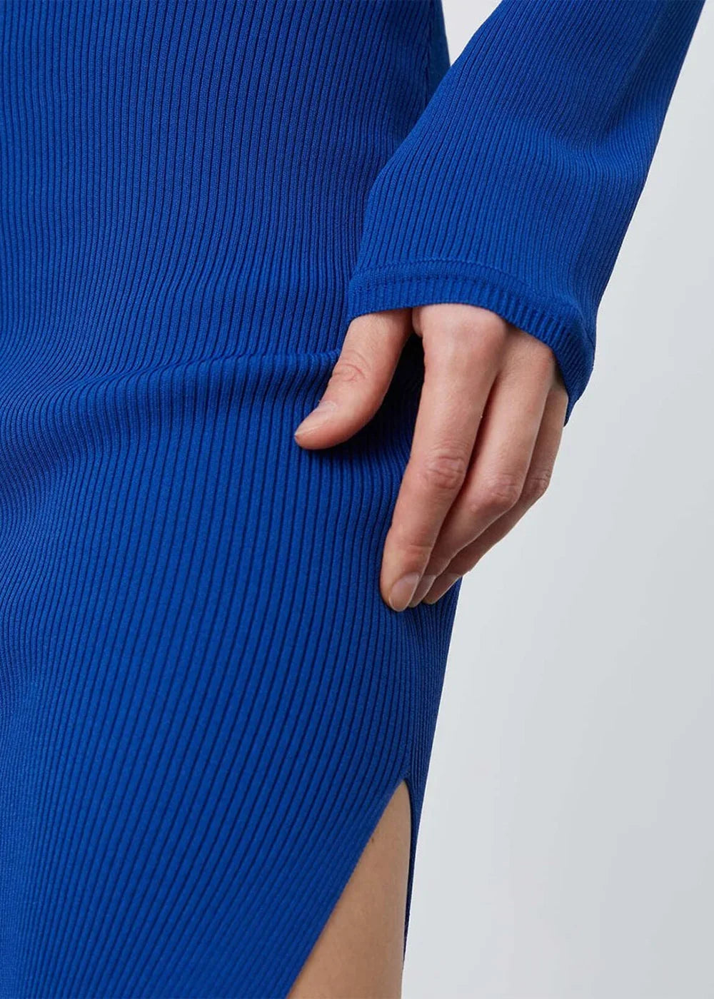 Close-up of a royal blue ribbed knit sweater dress with a side slit, showing a hand resting on the fabric.