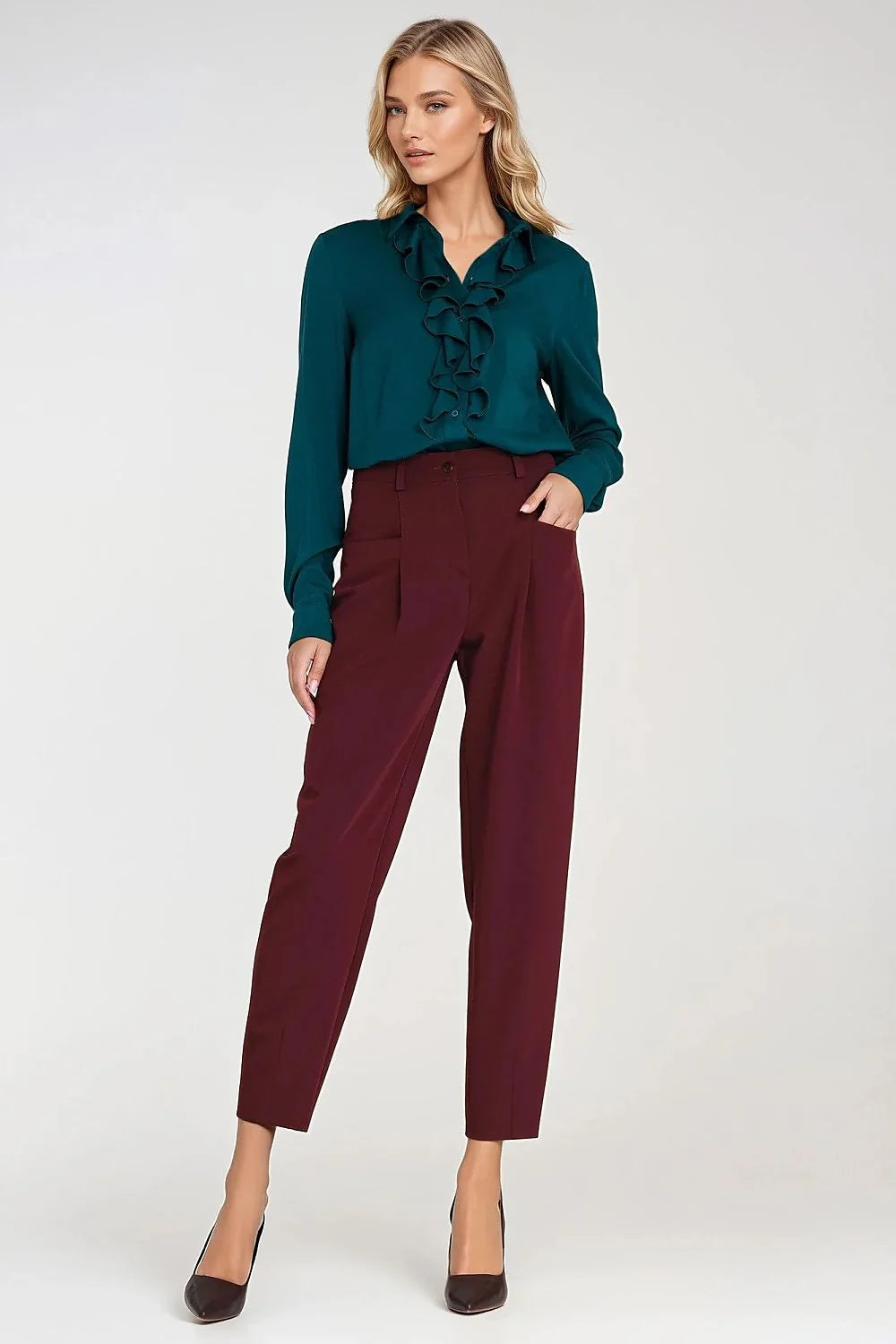 Model wearing a teal ruffled blouse and maroon high-waisted pants with black heels.